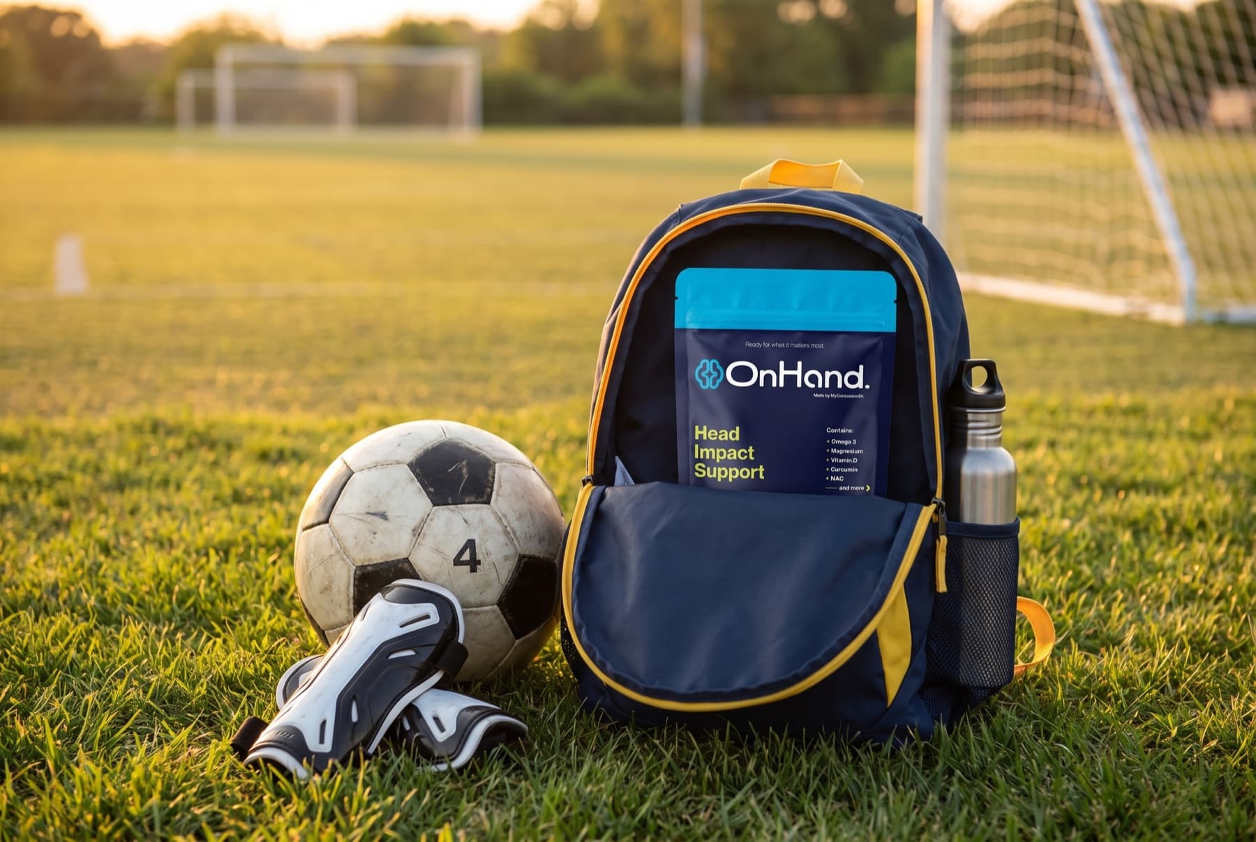 An OnHand pouch in a youth soccer backpack on the grass beside a ball and shin guards at golden hour