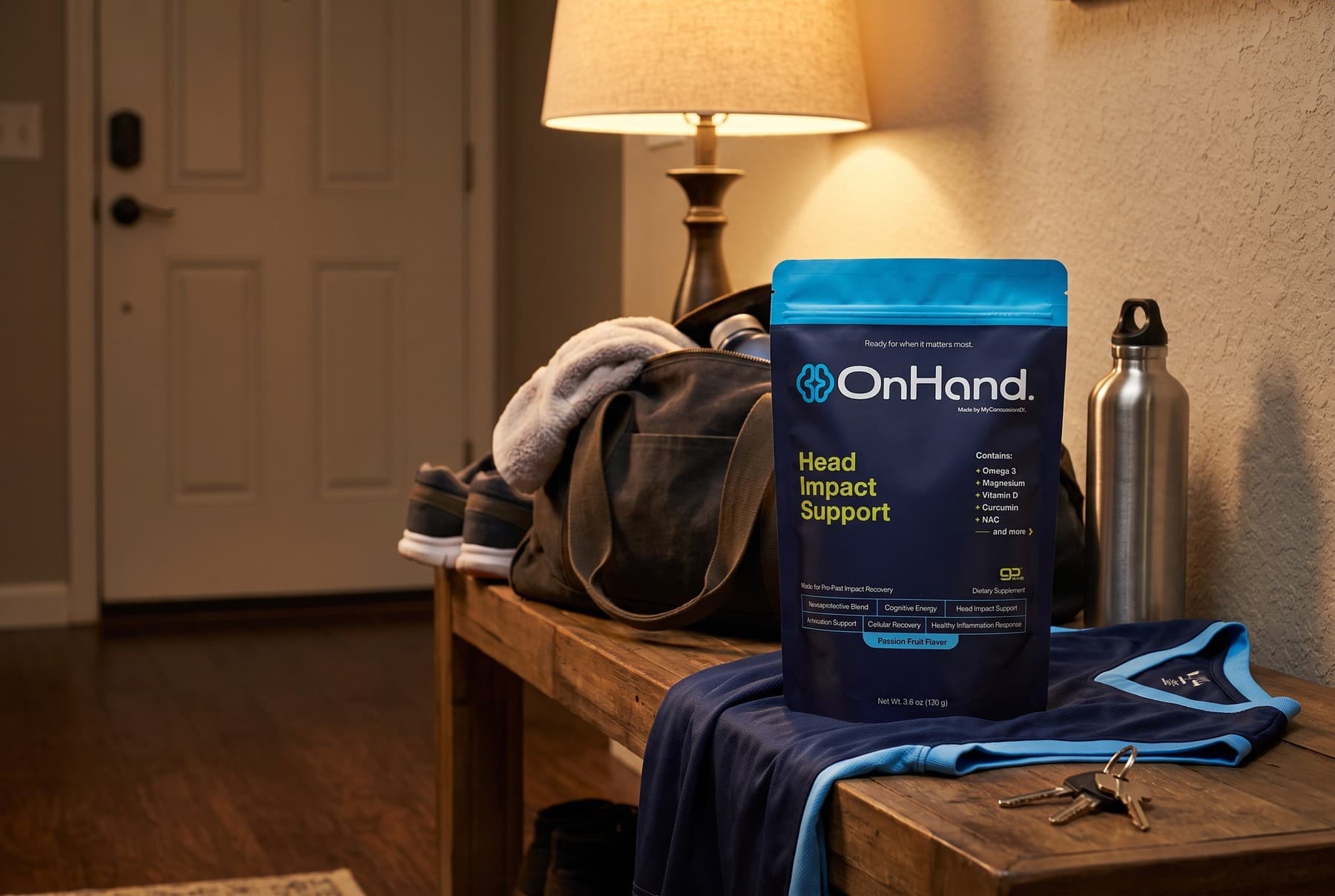 The OnHand pouch standing on a wooden hallway bench in the evening beside an unpacked gym bag, a folded jersey, a water bottle and house keys, under lamp light